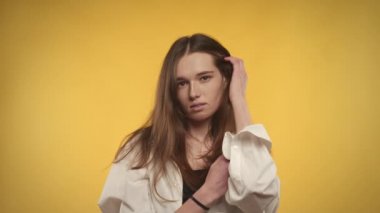 20 'li yaşlarda beyaz bir kadının parlak sarı bir arka planda kameraya gülümseyen portresi.