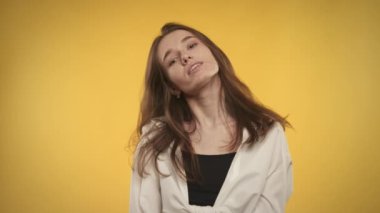 20 'li yaşlarda beyaz bir kadının parlak sarı bir arka planda kameraya gülümseyen portresi.