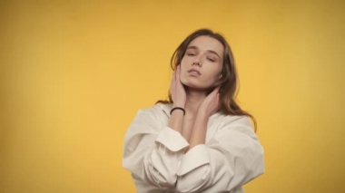 20 'li yaşlarda beyaz bir kadının parlak sarı bir arka planda kameraya gülümseyen portresi.