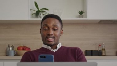 Mutlu, gülümseyen Afrikalı Amerikalı adam, arkadaşlarını evdeki bir bilgisayardan selamlıyor.