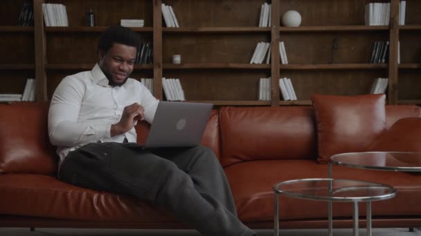 Dicisión haciendo hombre de negocios delante de su portátil en un sofá en su oficina loft — Vídeos de Stock