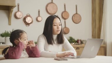 Asyalı anne ve kız evlerinde dizüstü bilgisayarın önünde sohbet ediyorlar.