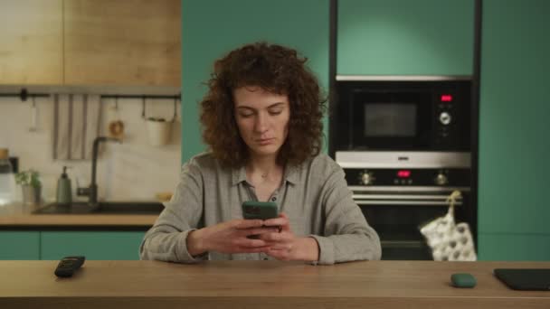 Young 20s adult student typing on her smart phone in her kitchen — Wideo stockowe