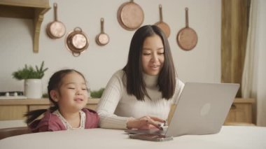 Young mother and daughter talking in front of a laptop indoors