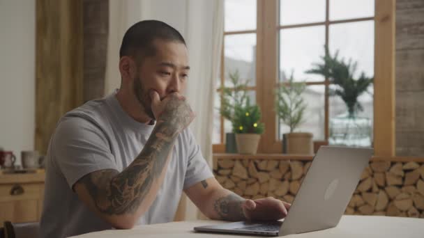 Young adult asian man takes a break to think on a solution in front of his laptop indoors — Vídeo de stock