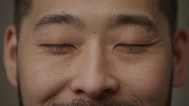 Ağır çekimde gülümseyen ve kameraya bakan Koreli bir adamın aşırı yakın çekimi.
