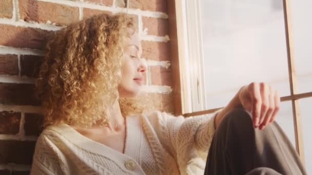 Młoda kręcone biały kobieta patrząc w w okno w jasnym słońcu — Wideo stockowe