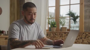 Genç, Asyalı bir adam bilgisayarının içinde çalışırken telefona cevap veriyor.