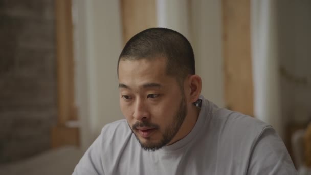 Närbild porträtt av en ung vuxen asiatisk man som får goda nyheter på sin bärbara dator inomhus — Stockvideo