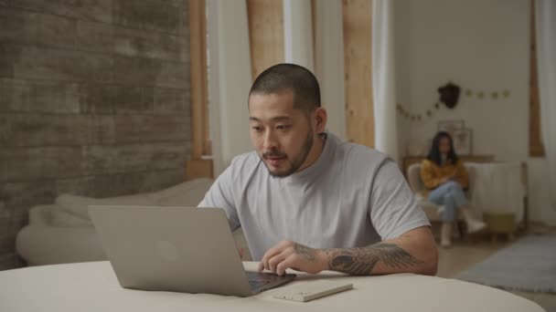 Close up portrait of a young adult asian man recieving good news on his laptop computer indoors — Stockvideo