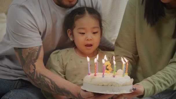 Девочка задувает свечу на торте в честь дня рождения, празднуя 3 года — стоковое видео