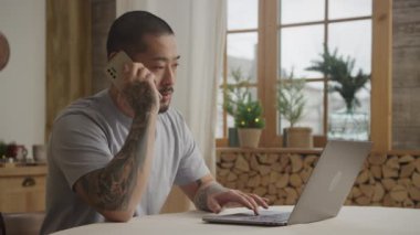 Genç, Asyalı bir adam bilgisayarının içinde çalışırken telefona cevap veriyor.