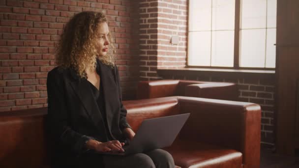 Jonge stijlvolle zakenvrouw werkt op een laptop in een loft appartement met rode bakstenen muur — Stockvideo