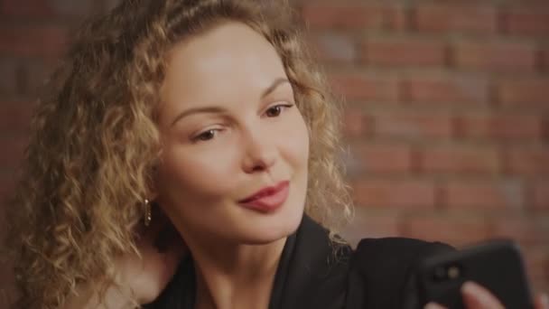 Porträt einer jungen lockigen kaukasischen Geschäftsfrau, die Selfies macht und mit roter Backsteinwand lächelt — Stockvideo