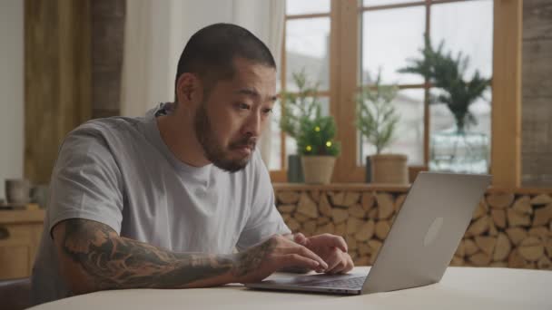 Um monte de várias expressões faciais por um homem asiático tatuado na frente de seu laptop — Vídeo de Stock