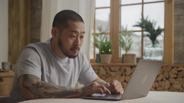 Um homem adulto asiático tottooed está navegando em seu laptop com várias expressões faciais — Vídeo de Stock