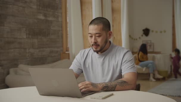 Ein Vater erhält schlechte Nachrichten auf seinem Laptop, während seine Frau und Tochter im Hintergrund spielen — Stockvideo