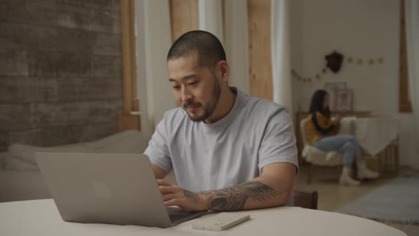 Glücklicher Vater arbeitet glücklich an seinem Laptop, während seine Frau im Hintergrund sitzt — Stockvideo
