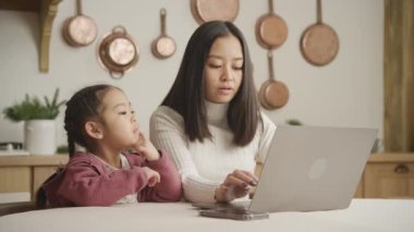 Annesi dizüstü bilgisayarı üzerinde çalışırken kızı eğleniyor.