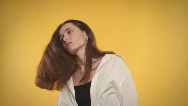 Молодая белая женщина трясет волосами и смотрит в камеру на ярко-желтом фоне — стоковое видео