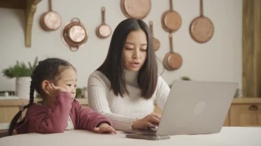 Annesi dizüstü bilgisayarı üzerinde çalışırken kızı eğleniyor.