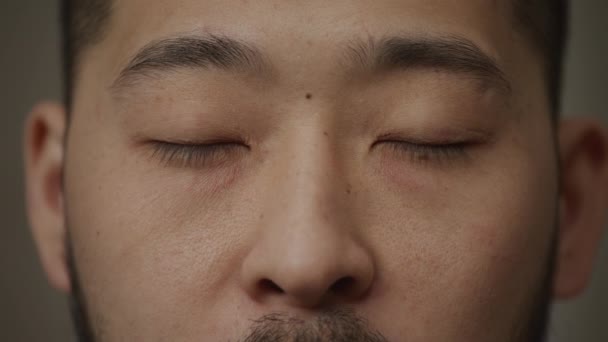 Tagträumende oder geschlossene asiatische Männeraugen mit einem Lächeln zwinkert aus nächster Nähe — Stockvideo