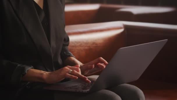 Mulher irreconhecível mãos vestidas com um terno moderno sentado em um sofá de couro e digitação — Vídeo de Stock