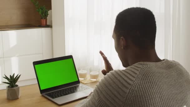 Giovane uomo afroamericano seduto di fronte a un computer portatile schermo verde su una videochiamata in un luminoso appartamento soleggiato — Video Stock