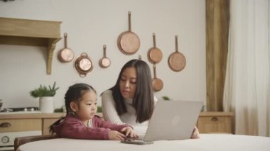 Genç Asyalı anne ve kızı laptoplarını karıştırıyor ve içeride konuşuyorlar.