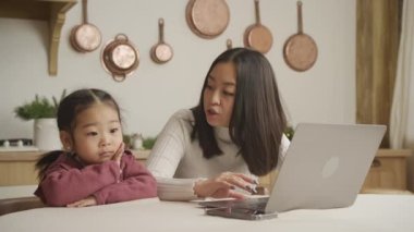 Asyalı anne ve kızı bilgisayarlarında internette geziniyor ve içeride konuşuyorlar.