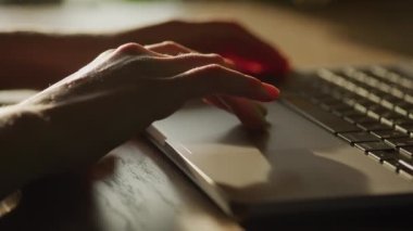 Kadın eli kareye giriyor ve ağır çekimde gün batımında dizüstü bilgisayarın dokunmatik bölmesinde yana doğru sekiyor.