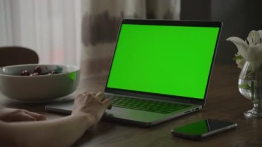 Kafkasyalı bir kadının laptopun üstünde elini dinlendirirken, yeşil ekran renkli dokunmatik anahtarı ağır çekimde.