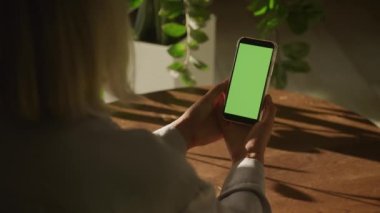 90 fps ağır çekimde omuzunda yeşil ekran krom anahtarı olan dikey akıllı telefonu tutan bir kadının el kamerasıyla çekilmiş fotoğrafı.