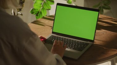 Handheld close up of a woman scrolling on a laptop computer touchpad with green screen chroma key indoors in slow motion