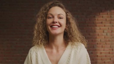 Genç, kıvırcık, beyaz bir kadının video kasetteki görüntüsü. Kırmızı tuğlalı duvarın içinde selamlaşır ve konuşurlar.