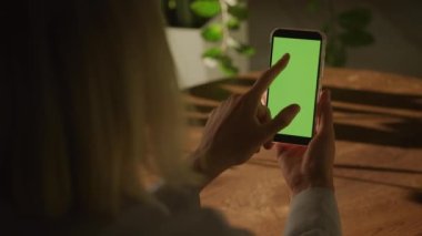 Elinde yeşil ekran krom anahtarı olan akıllı bir telefonu tutan ve 90 fps yavaş çekimde kapalı alanda tek bir geçiş yapan bir kadının el kamerası.