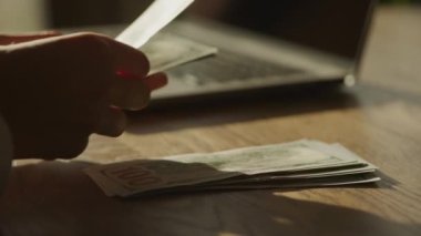 Handheld closee up of caucasian woman hands counting money in front of laptop computer in slow motion