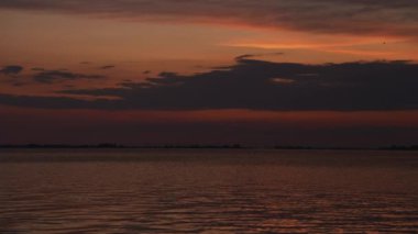 Gün batımındaki gökyüzünün üzerinde sakin bir su ve uzak bir kuş olan bir nehirde pürüzsüz bir kamera yansıması.