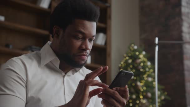 Gezichtsuitdrukkingen Van Een Afrikaanse Amerikaanse Man Browsen Smartphone Met Kerstboom — Stockvideo