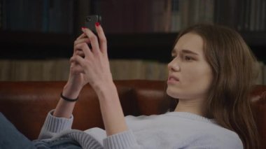 Close up caucasian woman typing or texting on her smart phone with various facial expressions in slow motion indoors