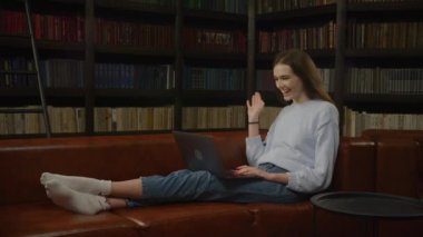 Caucasian woman student waving her hand in a greeting during a video call with friends on her laptop computer indoors in slow motion