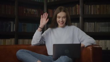 Caucasian student woman waving hand in a greeting gesture on a video call on her laptop indoors