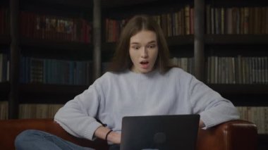Young adult caucasian woman receiving shocking news on her laptop computer indoors in slow motion