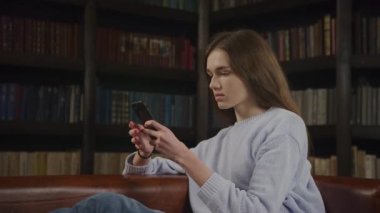 Optical zoom out caucasian woman browsing online on her smart phone showing various facial expressions indoors in slow motion