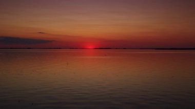 Red sunset over a calm river during summertime with a seagull flying by in distance