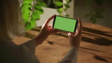 Handheld close up woman holding horizontal smart phone watching green screen chroma key indoors in 90fps slow motion