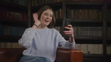Caucasian student woman waving hand in a greeting gesture on a video call on her laptop indoors
