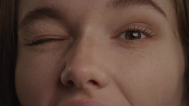 Close up of a caucasian woman eyes in a wink or blink gesture in slow motion indoors