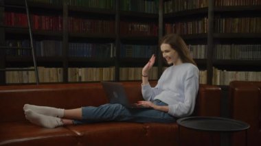 Caucasian woman student waving her hand in a greeting during a video call with friends on her laptop computer indoors in slow motion