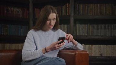 Close up of a caucasian woman browsing on her smart phone thoughtful in doubt indoors in slow motion